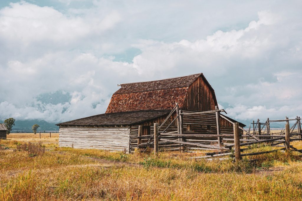 A century-old weathered timber barn standing in an open field under a heavy sky