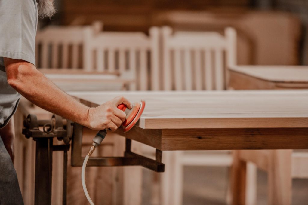 A craftsman running an orbital sander along the edge of a hardwood table top
