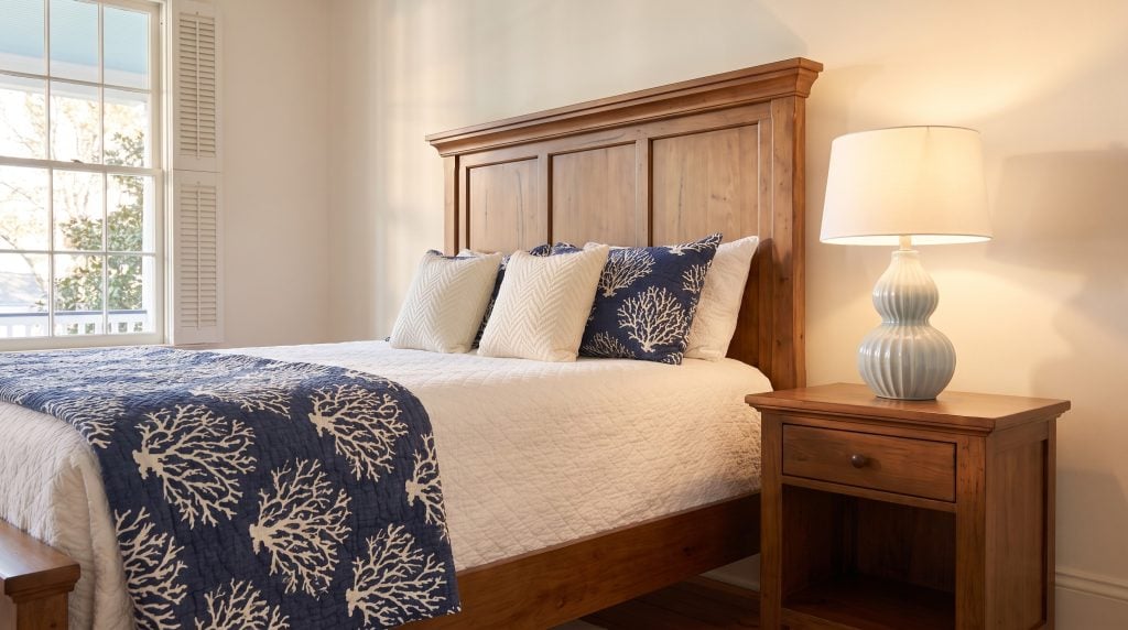 A paneled wood headboard and matching nightstand sit in a bedroom dressed with navy coastal bedding.