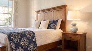 A paneled wood headboard and matching nightstand sit in a bedroom dressed with navy coastal bedding.