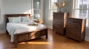 A brown maple panel bed with square posts, two tall chests of different heights and a three-drawer nightstand, in an I'On raised porch house in Mount Pleasant.