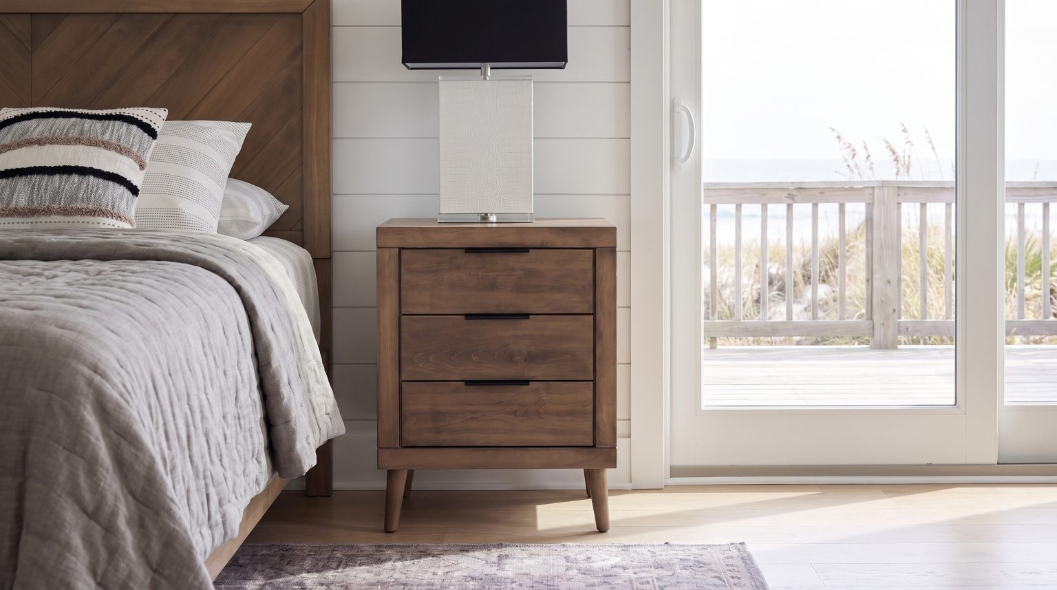 The nightstand: Three drawers with black bar pulls on round tapered legs.