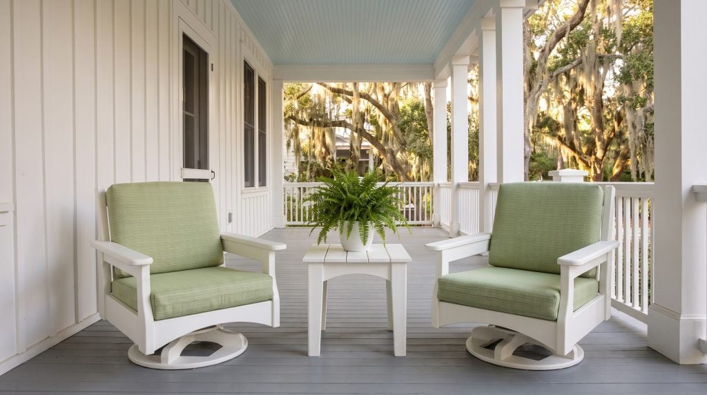 Two white poly lumber club chairs on swivel glider bases with celery green cushions, and a square side table, on a Sullivan's Island porch.