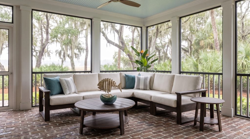 An L-shaped poly lumber sectional with thick white canvas cushions on a dark brown frame, with round coffee and side tables, on a Kiawah screened porch.
