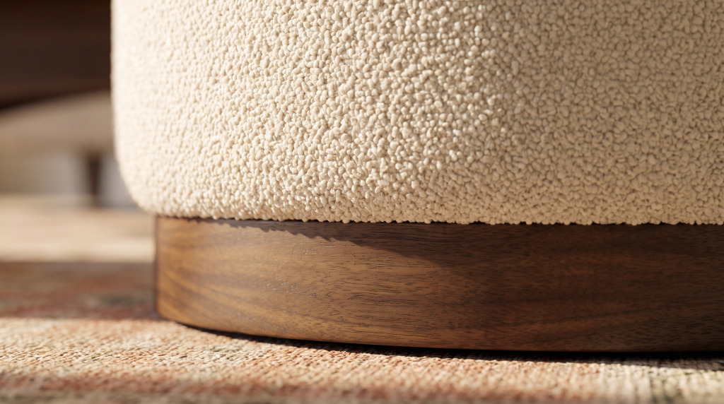 A close view of cream boucle upholstery meeting the plain wood plinth base of a round ottoman