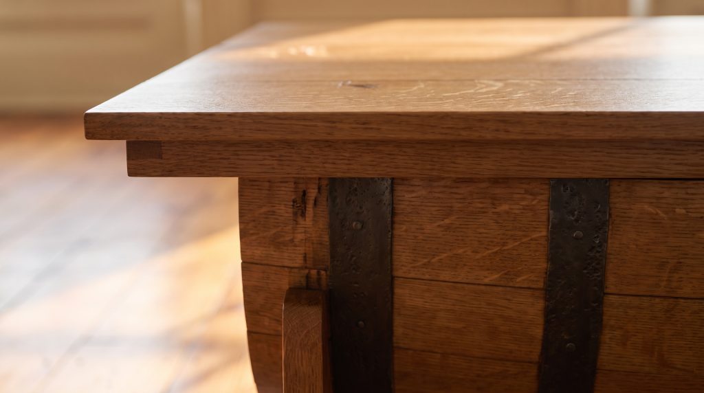 A close view of a straight oak table edge oversailing curved barrel staves bound by a dark forged iron hoop