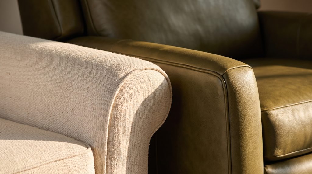 A close view of a cream sofa arm with self-welt piping meeting the pebbled grain of an olive leather chair arm