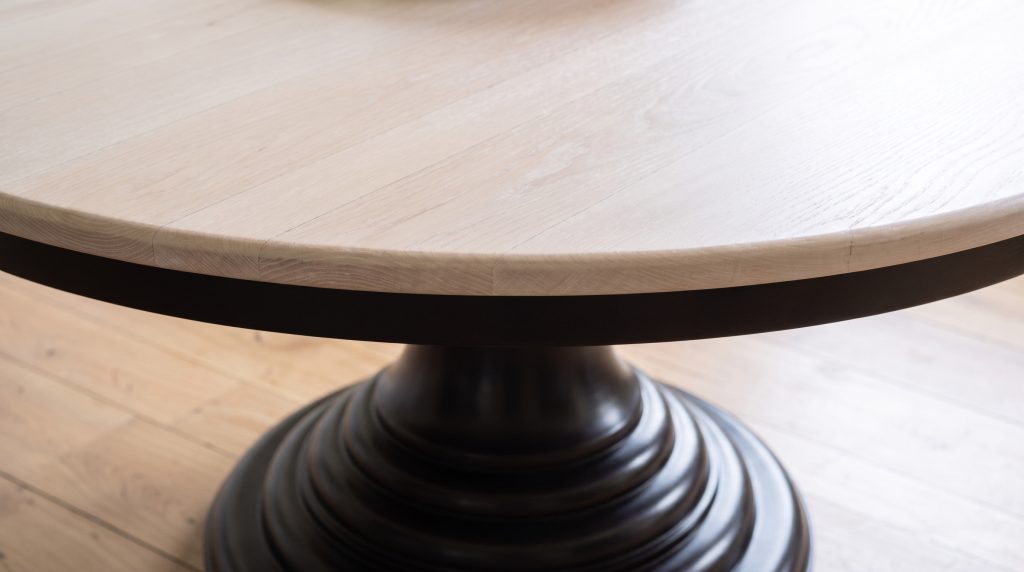 A close view of a pale bleached maple table edge sitting directly above the first collar of a near-black turned pedestal