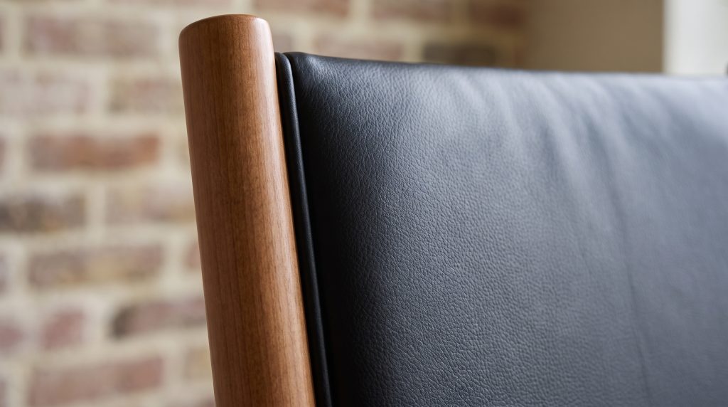 A close view of a padded black leather back panel tucked into a shallow rebate in a warm brown maple stile