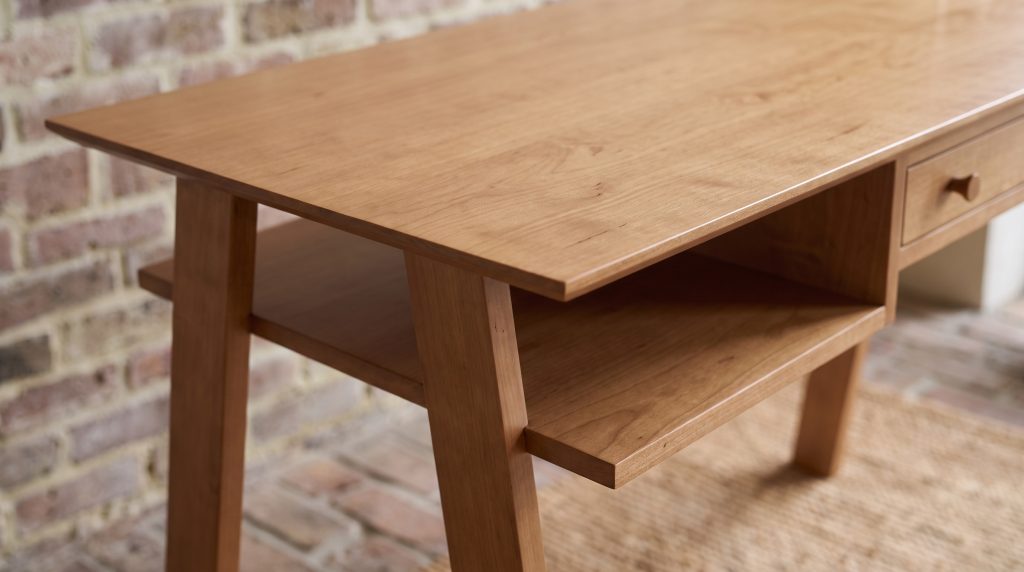 A close view of a maple desk corner where a knife-thin beveled top edge meets the shoulder of an outward-raking leg