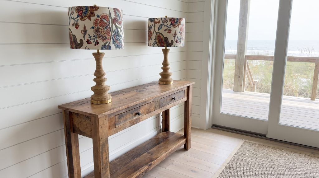 A reclaimed oak console table with two drawers and a lower shelf against painted shiplap, with a pair of rope-wrapped lamps and printed shades