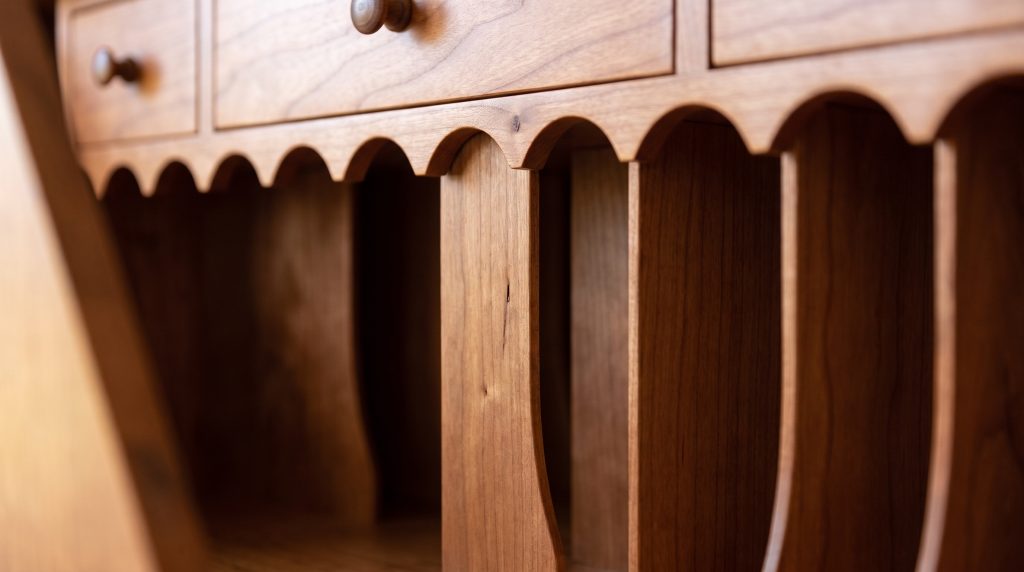 A close view of thin cherry letter dividers forming narrow empty pigeonholes beneath a valance cut into shallow arches