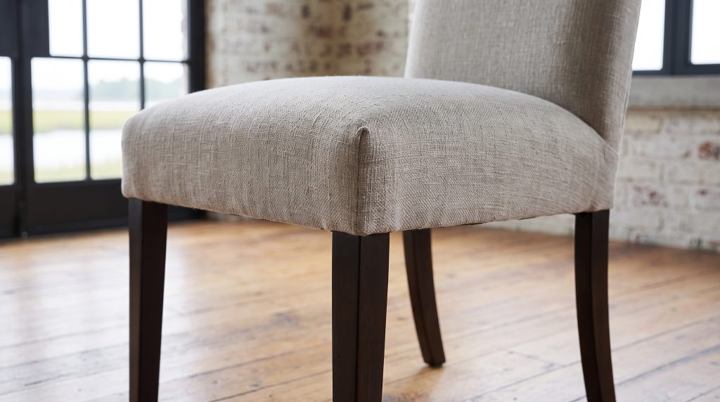A close view of the greige upholstered seat corner of a parsons chair over a near-black tapered leg