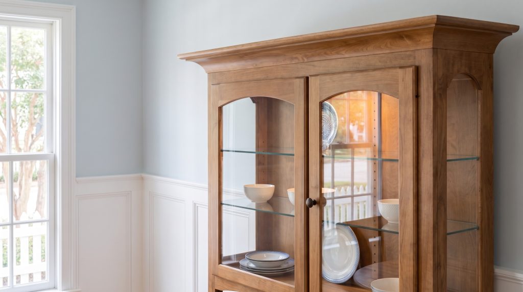 An arched glass door in honey maple with a small bronze knob, glass shelves behind.