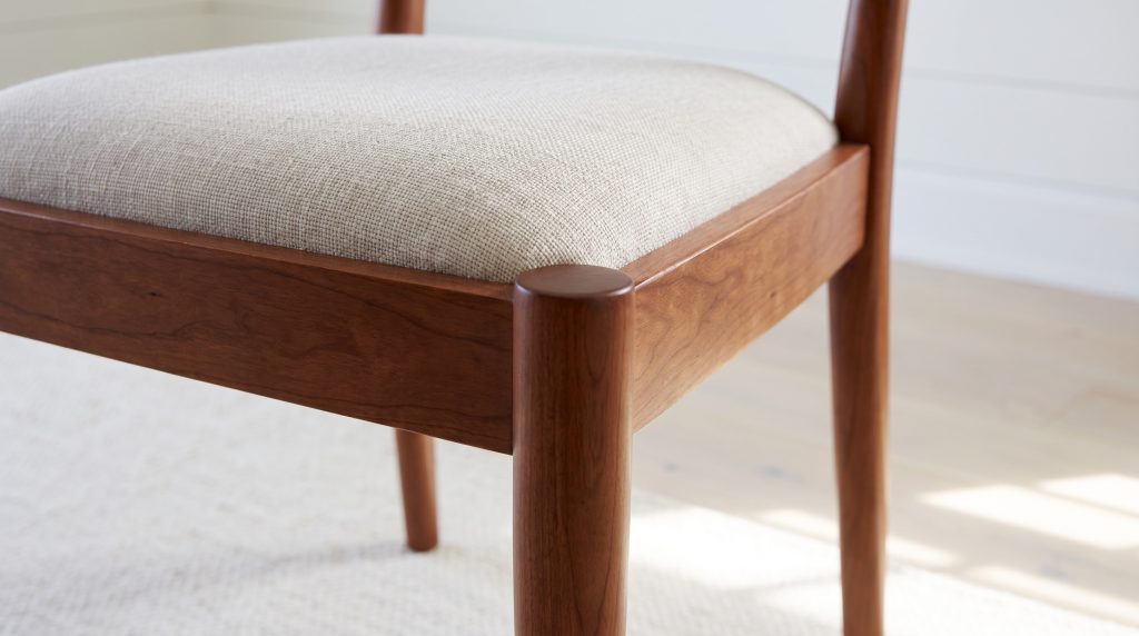A round end-cap at the front corner of the seat frame, under a woven oatmeal seat.