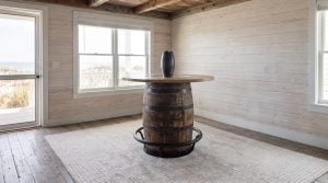 A charred barrel base with riveted hoops and a steel footrest ring, under a round oak top.