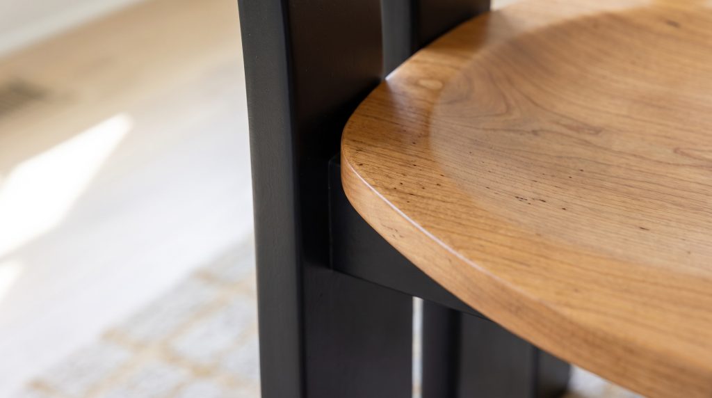 A close view of a honey maple chair seat meeting a flat black painted upright