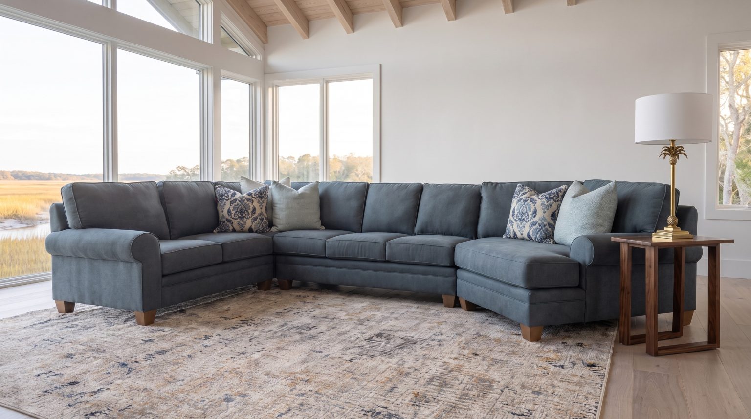 A slate-blue sectional corner and cuddler end with a walnut sled end table and brass palm lamp, marsh glazing behind