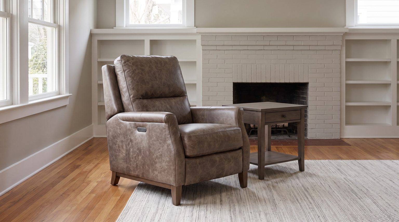 A mottled taupe leather power recliner beside a smoke maple end table and a painted brick fireplace