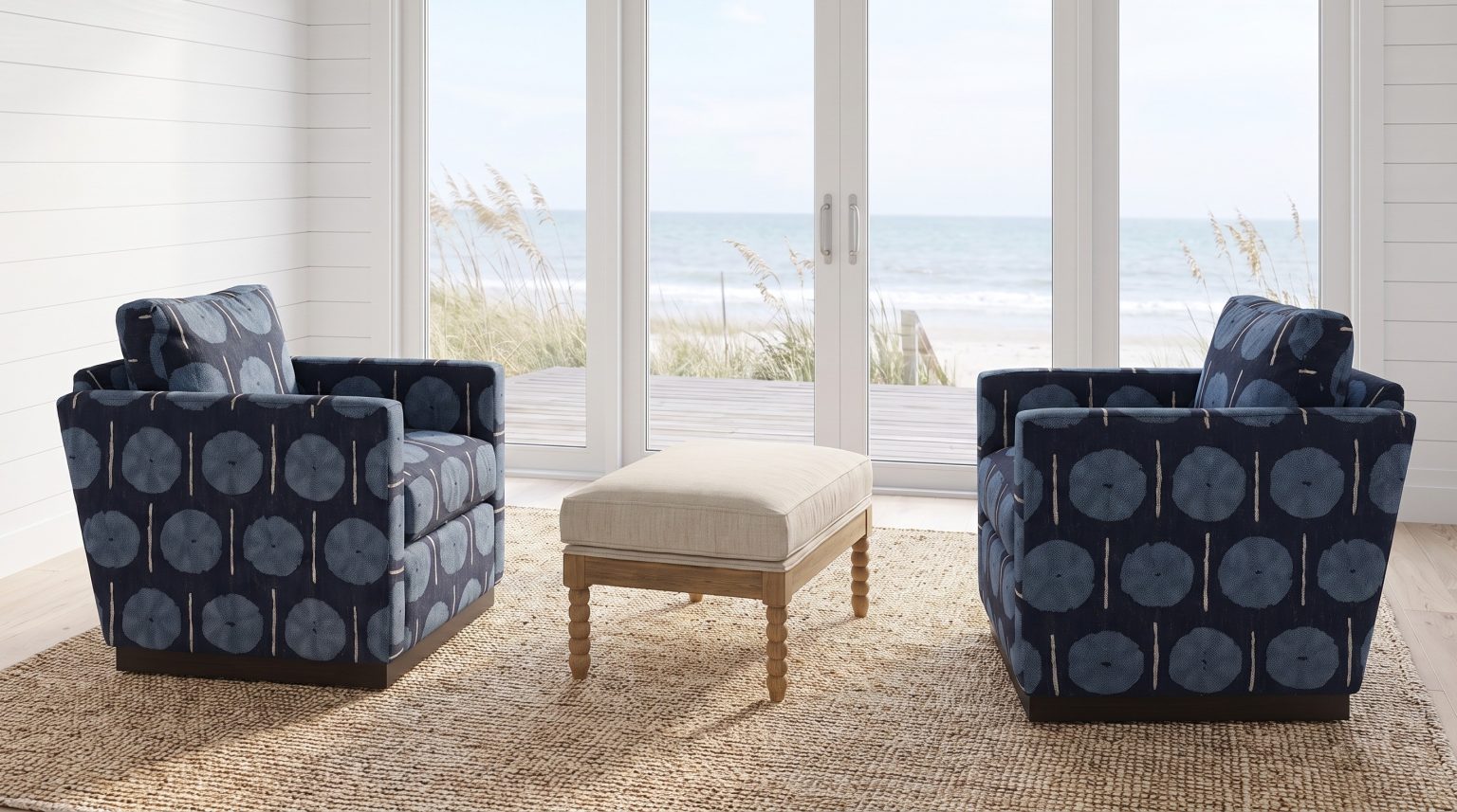 Two navy swivel chairs with sky-blue medallions facing across a linen ottoman, ocean beyond