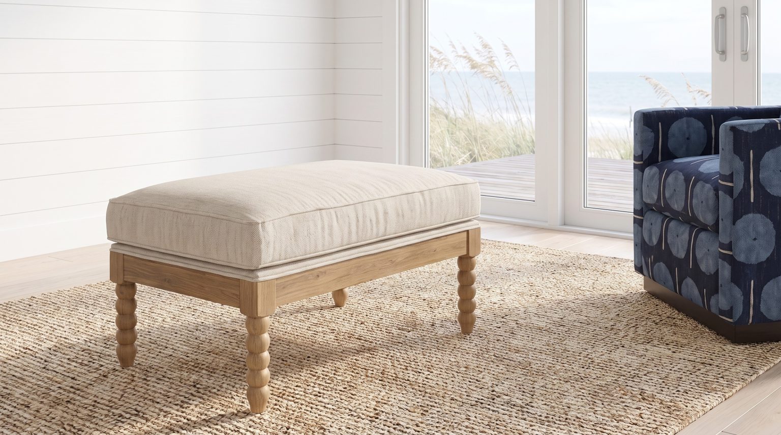 A linen ottoman on natural bobbin-turned legs on a jute rug beside a navy print chair