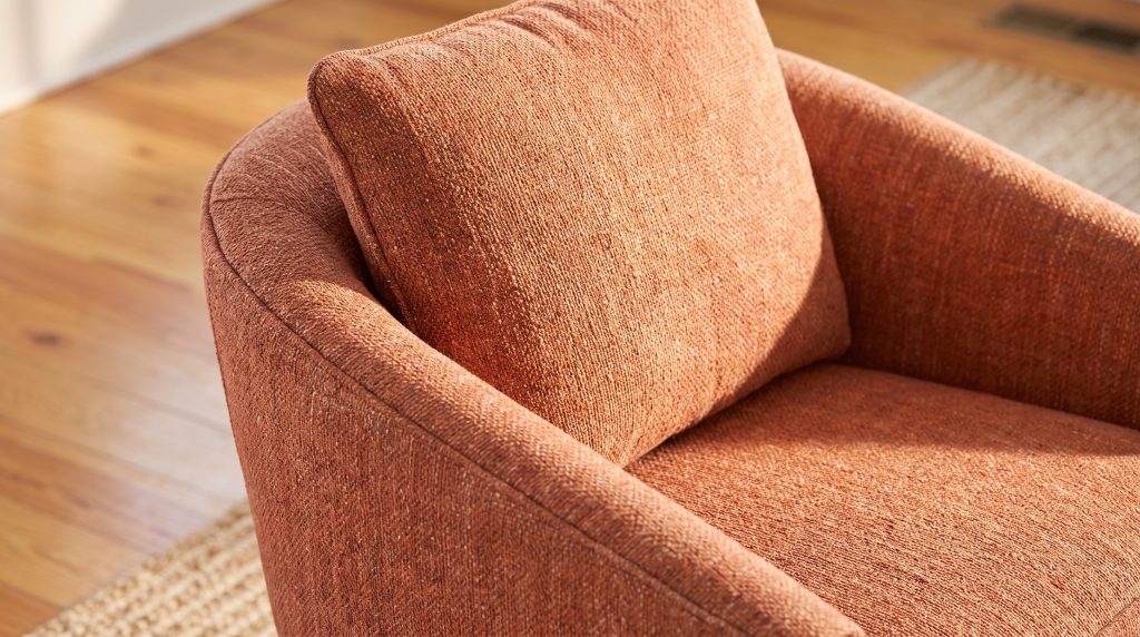 A close view of flecked terracotta fabric where a barrel chair back curves into the arm