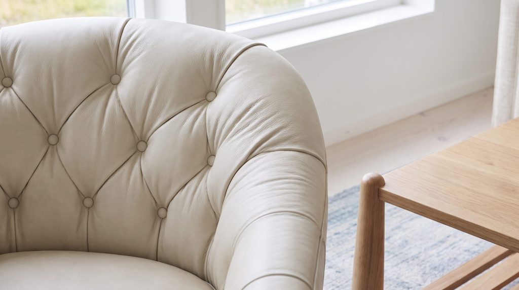 Close-up of a buttoned cream tufted chair back beside the light oak frame of a coffee table