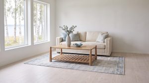 A cream sofa behind a light oak coffee table with a slatted lower shelf on a pale gray-blue rug
