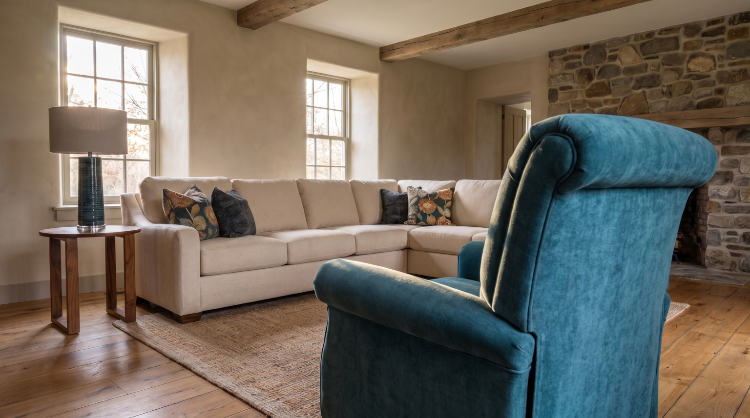 A teal recliner in the foreground with the cream sectional and deep-set windows behind it