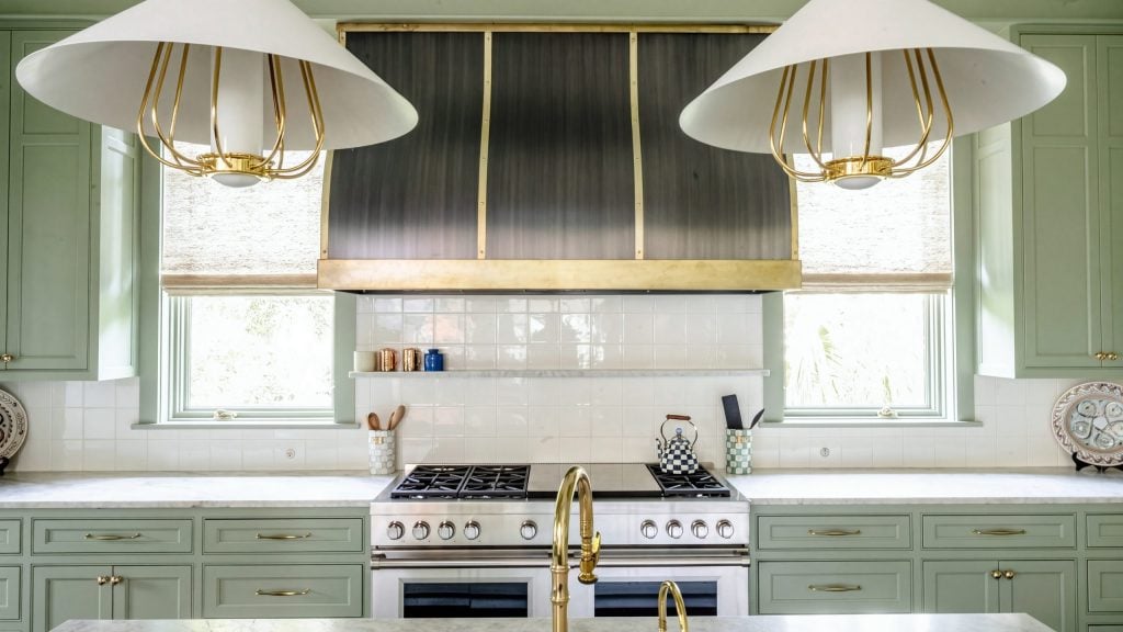 Hood and pendants: The brass-strapped hood between two windows, over sage base cabinets.