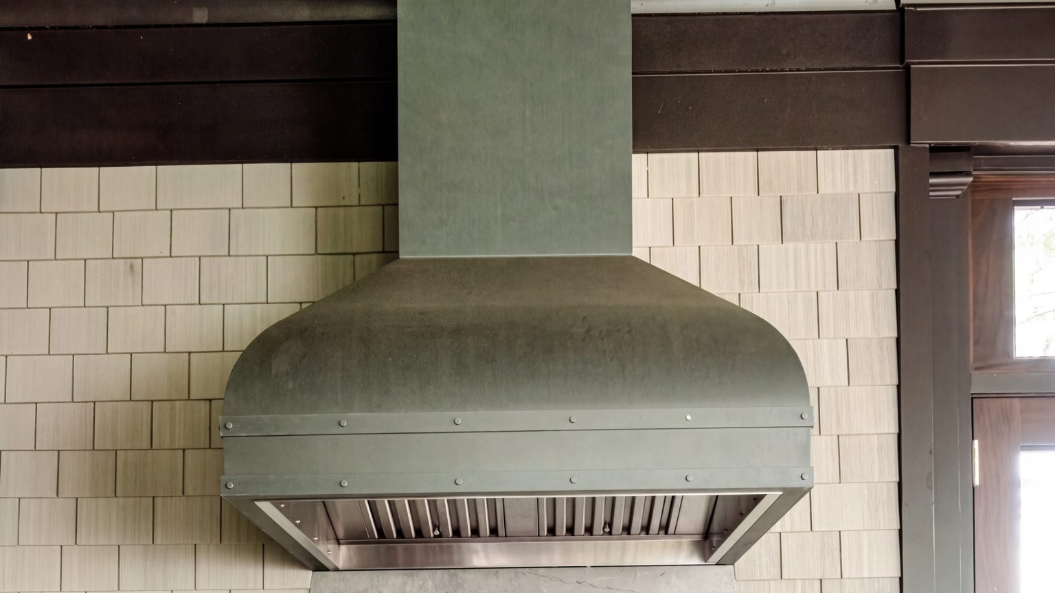 The hood: a banded, riveted hood over a soapstone backsplash cut in a bell curve, against shingled porch walls.