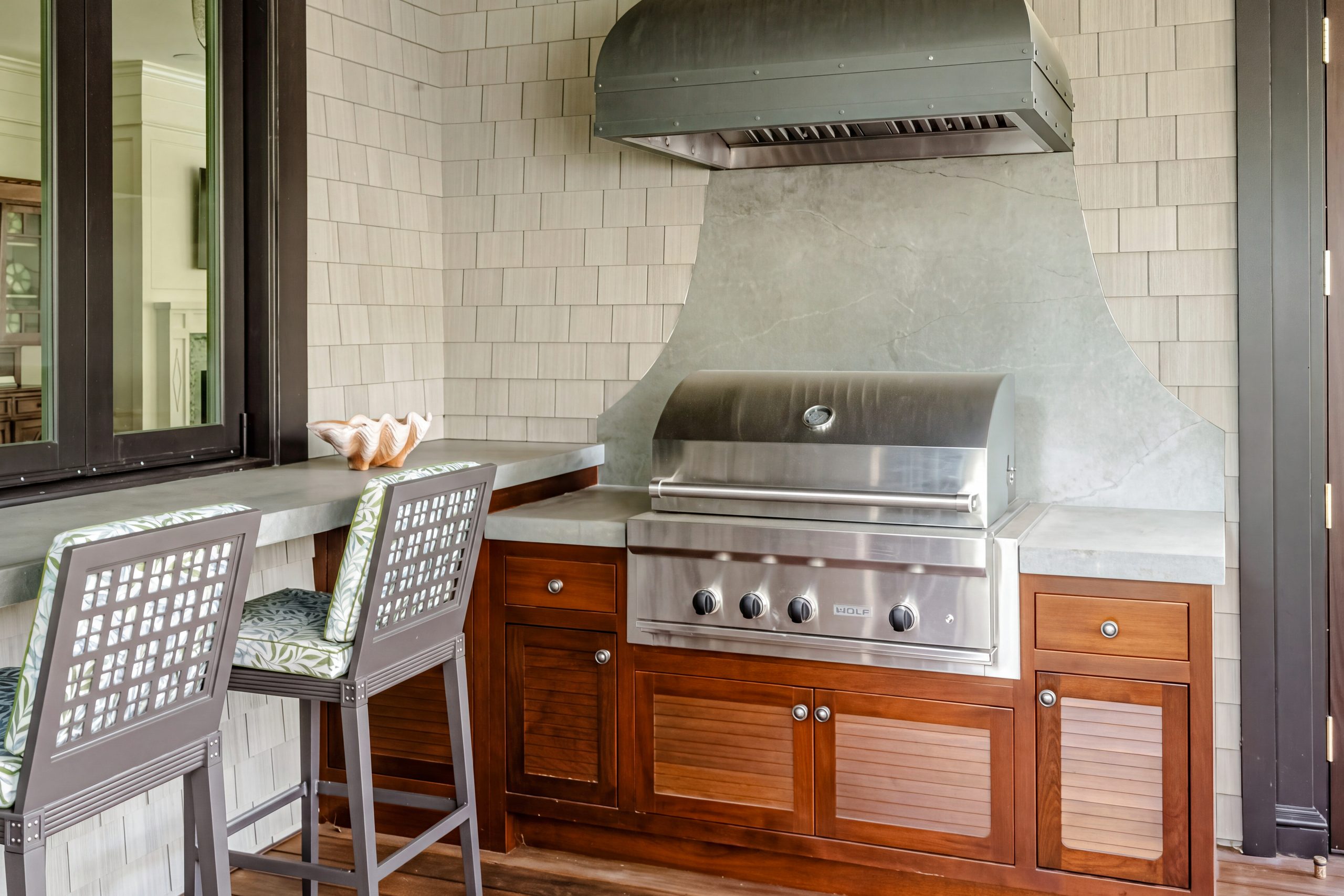 Mahogany outdoor kitchen cabinets with louvered doors under a shaped gray soapstone backsplash and a built-in grill on a Kiawah Island screened porch.