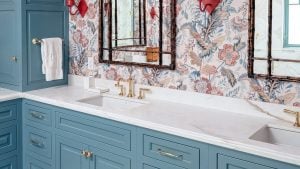 Sink run and tower: a slate-blue inset vanity turns past a paneled linen tower, with brass faucets on a white marble top.