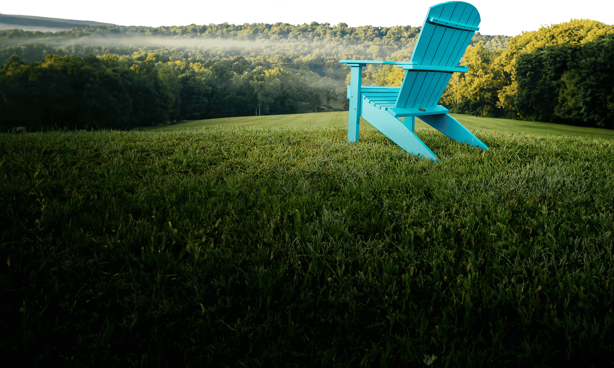 A single Aruba Blue poly Adirondack chair on a mown hillside at first light, mist over the treeline