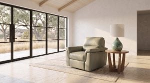 A sage green leather chair beside a small round oak end table with a ceramic lamp at a glass wall