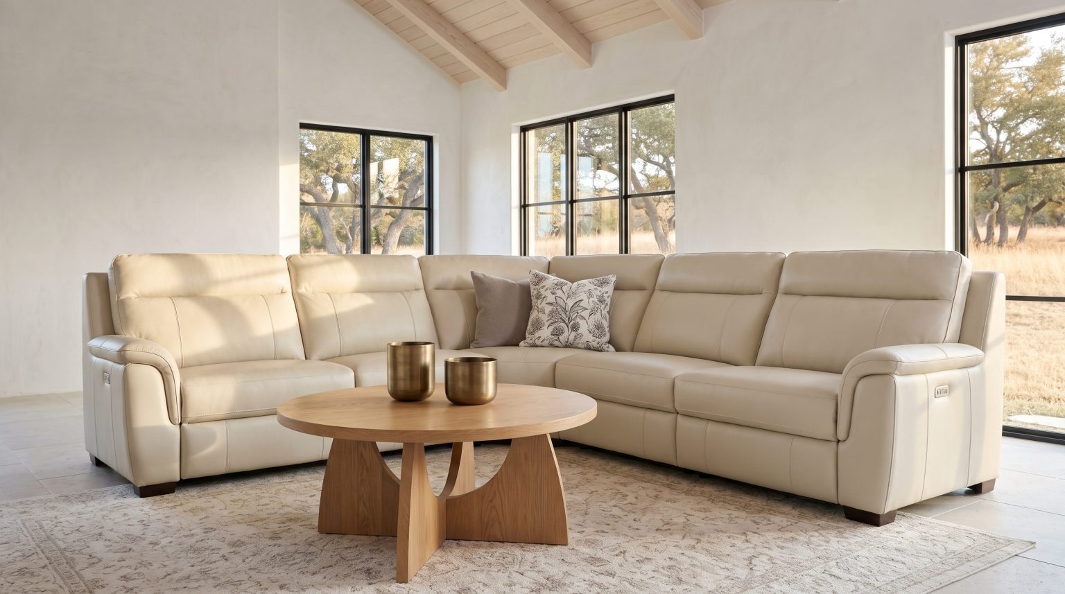 A cream leather reclining sectional wrapping a corner behind a round oak pedestal coffee table