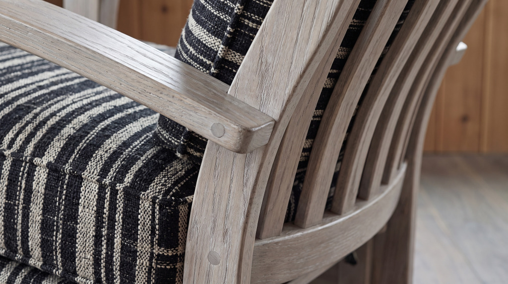 A close view of a black and cream woven stripe meeting the shaped weathered oak arm of a glider, with a peg covering the joint