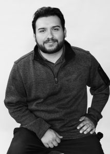 Warehouse technician Alex Villarreal smiles for a black-and-white studio portrait.