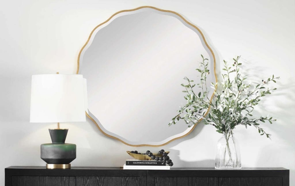 A ceramic table lamp and a scalloped gold-framed mirror above a dark wood console