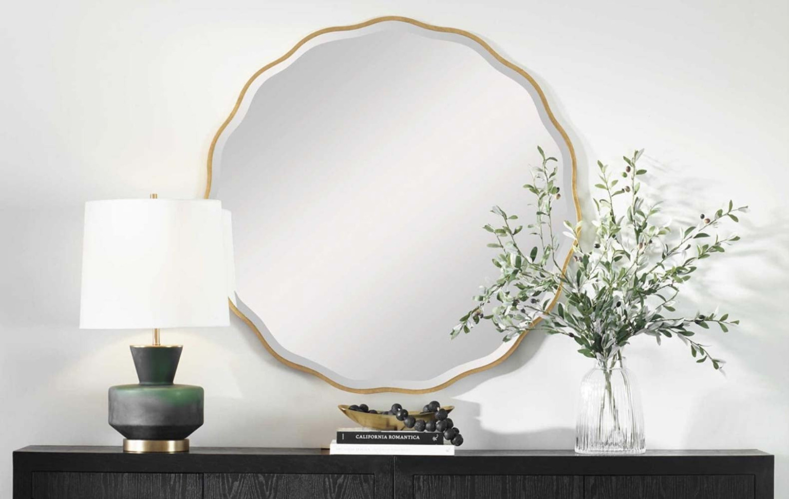 A ceramic table lamp and a scalloped gold-framed mirror above a dark wood console
