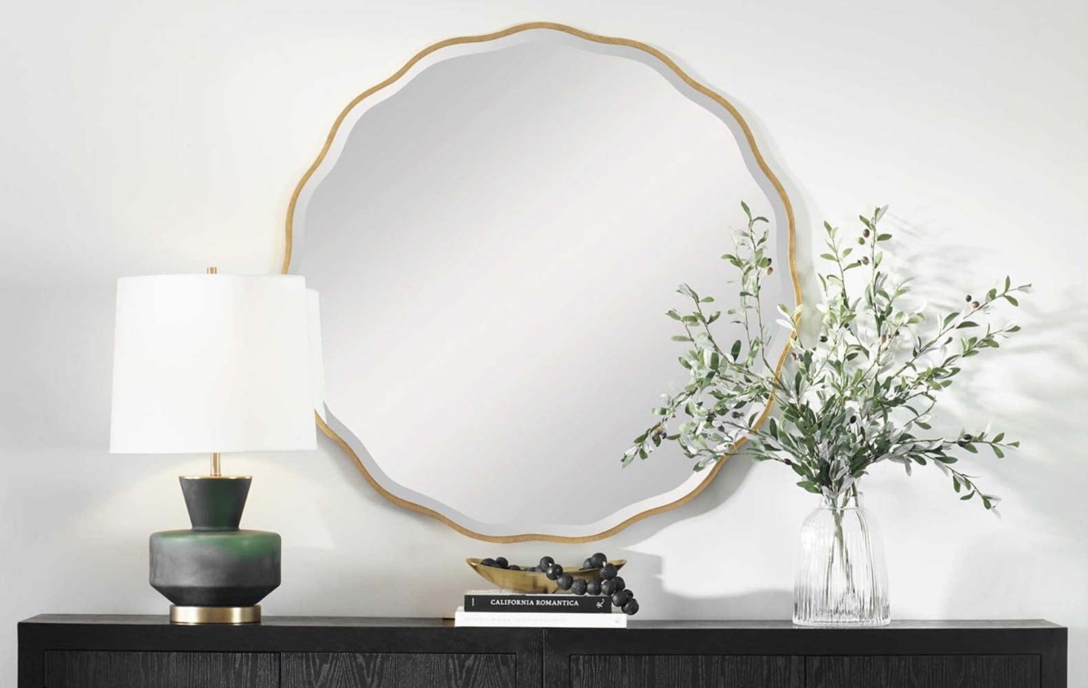 A ceramic table lamp and a scalloped gold-framed mirror above a dark wood console